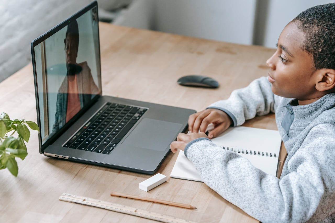 From above side view of crop African American schoolchild watching netbook with speaking female teacher during distance learning at table